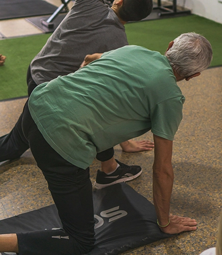 Senior on yoga mat stretching in front of man